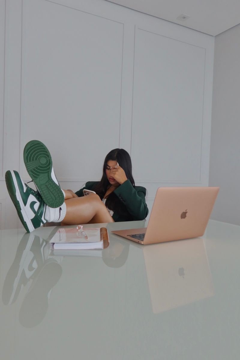 Sneakers verdes e brancos em um look com blazer verde, em uma mesa de trabalho